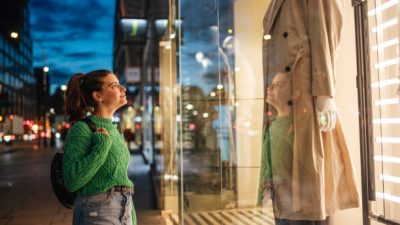 Young woman looking at store display at night in the city.